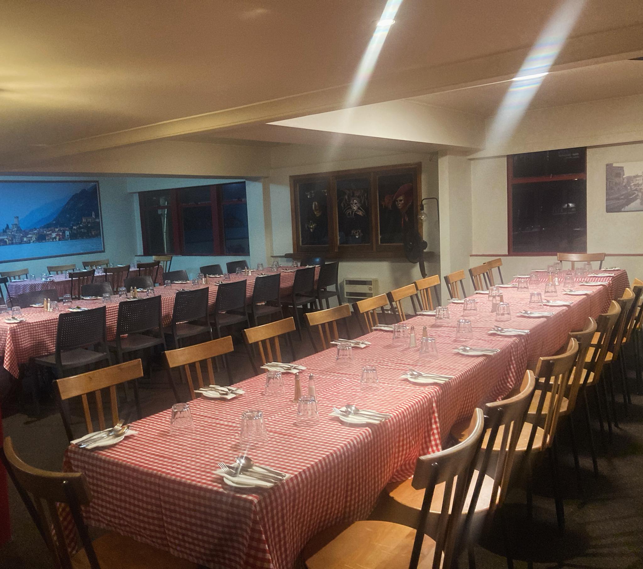 The upstairs room set with long gingham tables and a painted lake view on the wall